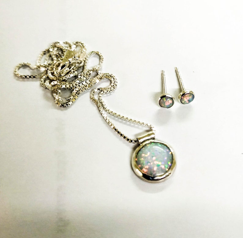 May include: A silver necklace with a round opal pendant and matching opal earrings. The opal is a milky white color with flashes of green and blue.