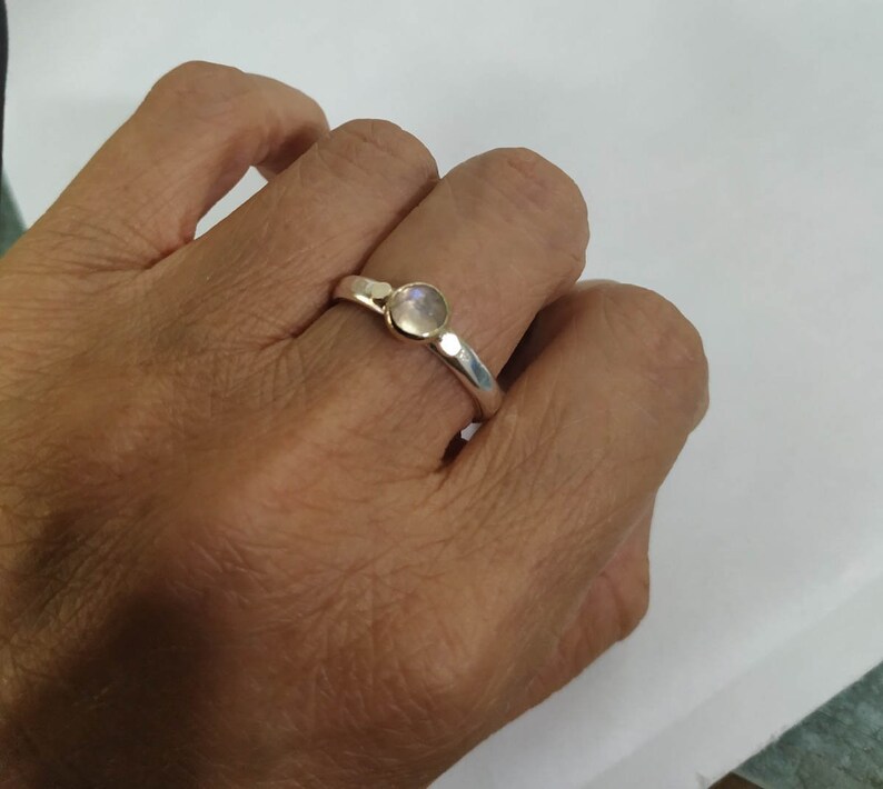 May include: A silver ring with a round, clear gemstone set in the center. The ring is worn on a person's finger.