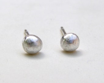 May include: A pair of silver stud earrings with a brushed finish. The earrings are round and have a slightly domed shape.