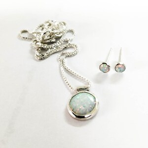 May include: A silver necklace with a round opal pendant and matching opal stud earrings. The necklace has a delicate chain.