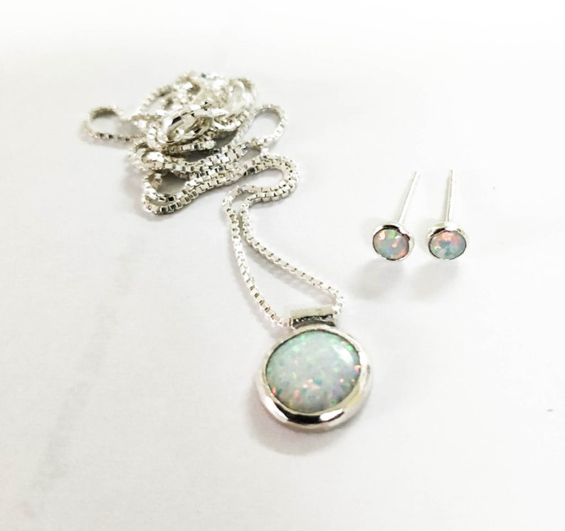 May include: A silver necklace with a round opal pendant and matching opal stud earrings. The necklace has a delicate chain.