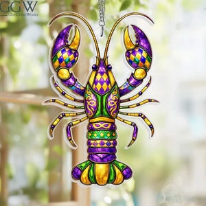 Op de afbeelding: Een kleurrijk kreeftornament met een Mardi Gras-thema. De kreeft heeft paarse, groene en gouden accenten met een ruitpatroon op de klauwen. Het ornament hangt aan een zilveren ketting.