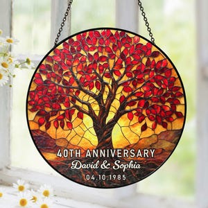 May include: Circular stained glass panel depicting a tree with red leaves and a brown trunk. The panel is inscribed with "40TH ANNIVERSARY", the names "David & Sophia", and the date "04.10.1985". It is suspended by a chain.