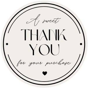 May include: A circular sticker with a cream background and black border. The text reads A sweet THANK YOU for your purchase in a mix of serif and script fonts. A small black heart is centered at the bottom, and two black dots are on the sides.