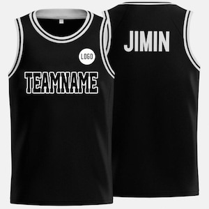 May include: Black basketball vest with white trim and accents. The front features the text "TEAMNAME" and a circular "LOGO" graphic. The back displays the name "JIMIN" in white block letters. The vest has a white and black neckline.