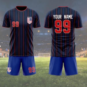 May include: A navy blue soccer jersey and shorts set. The jersey features red and blue vertical stripes, the number 99, and a US flag emblem. The shorts are blue with the number 99. The back of the jersey has the text "YOUR NAME" and the number 99.