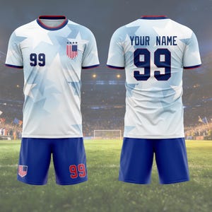 May include: A white and blue soccer uniform with the number 99 on the front and back. The jersey has a star pattern and a US flag crest. The shorts are blue with the number 99 on the right leg. The text "YOUR NAME" is above the number on the back.