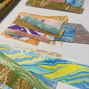 May include: A collection of colorful marbled paper scraps in various sizes and patterns. The paper has a swirling, abstract design with shades of blue, green, yellow, and brown.