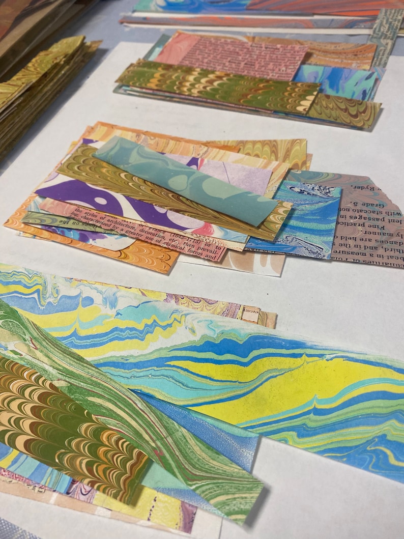 May include: A collection of colorful marbled paper scraps in various sizes and patterns. The paper has a swirling, abstract design with shades of blue, green, yellow, and brown.