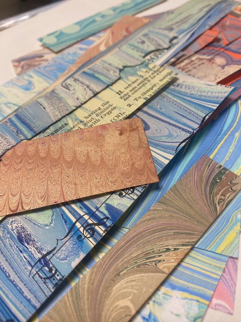 May include: A stack of colorful marbled paper sheets with a blue and white sheet with musical notes printed on it. The top sheet has text printed on it that reads "II. intrans. 1.T Eche man sotildh And colourethit It is novacience for 2. To tamper; meddie".