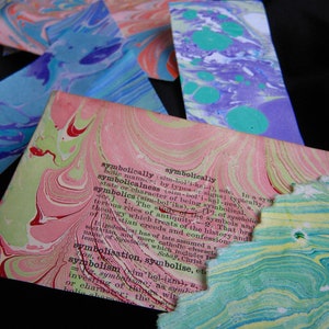 May include: A close-up of a page from a book with the word "symbolically" highlighted in pink and red. The page is made of marbled paper with a pink, green, and white pattern.