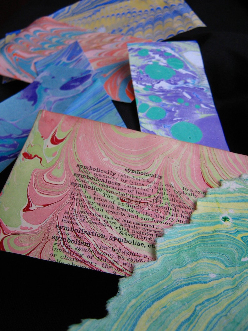 May include: A close-up of a page from a book with the word "symbolically" highlighted in pink and red. The page is made of marbled paper with a pink, green, and white pattern.