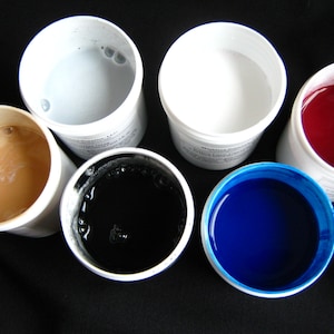 May include: Six small white containers with lids, each containing a different colored liquid. The colors are light gray, white, red, black, and blue.