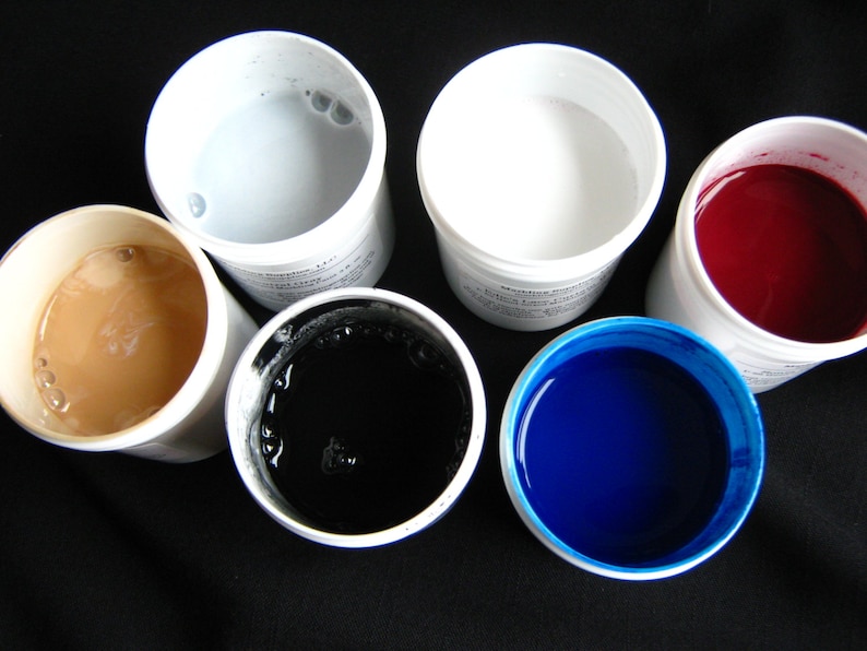 May include: Six small white containers with lids, each containing a different colored liquid. The colors are light gray, white, red, black, and blue.
