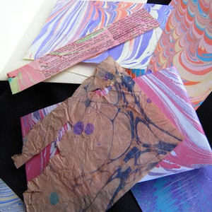 May include: A collection of colorful marbled papers in various shades of pink, blue, and white. The papers are arranged in a random pattern and have a unique, textured surface.