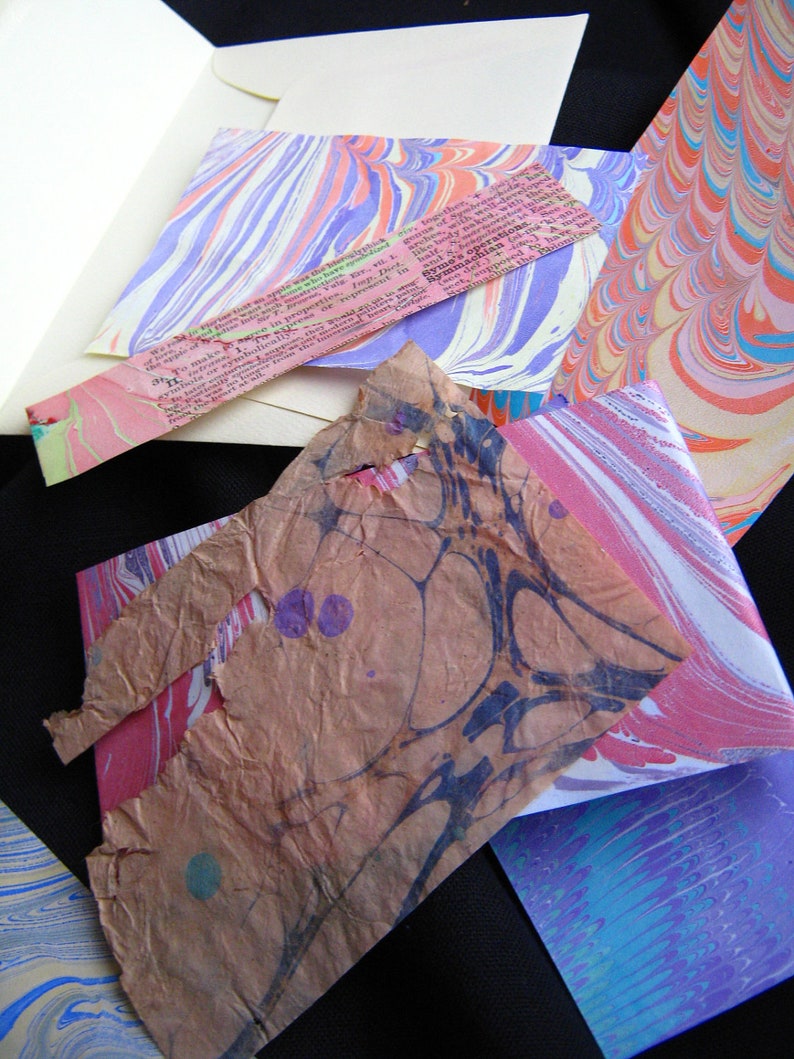 May include: A collection of colorful marbled papers in various shades of pink, blue, and white. The papers are arranged in a random pattern and have a unique, textured surface.