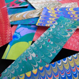 May include: A close-up of colorful marbled paper, with swirls of blue, green, red, yellow, and white. The paper is cut into strips and arranged in a layered pattern.