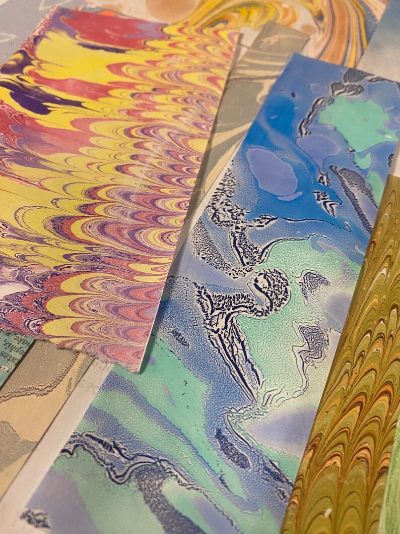 May include: Close-up of four different marbled paper samples. The papers are in shades of yellow, red, blue, green, and white. The marbling is intricate and detailed.