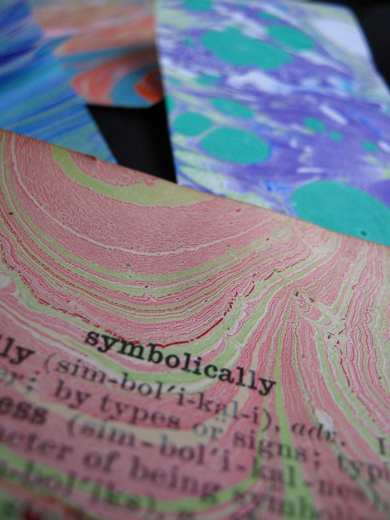 May include: Close-up of a dictionary page with the word "symbolically" defined. The page has a pink and green marbled pattern.