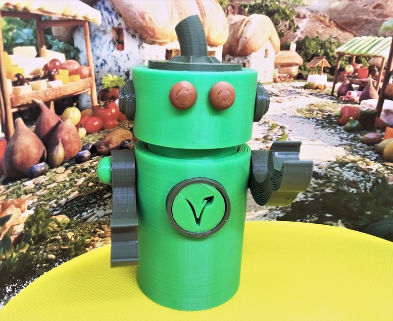 May include: A green robot figurine with brown eyes and a circular emblem with a V-shaped design. The robot has a cylindrical body, arms, and a head with a rounded top. The background features a colorful, whimsical scene.