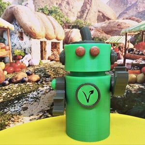 May include: A green robot figurine with brown accents, including circular eyes and a circular emblem with a plant symbol. The robot has a cylindrical body and is set against a colorful, whimsical background.