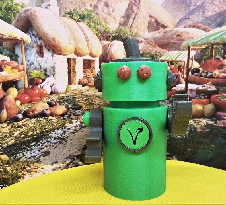 May include: A green robot figurine with brown accents, including circular eyes and a circular emblem with a plant symbol. The robot has a cylindrical body and is set against a colorful, whimsical background.