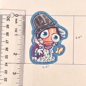 Pode incluir: Um autocolante extravagante com uma personagem de desenho animado com grandes olhos azuis, usando uma cartola e um casaco vermelho. O autocolante tem aproximadamente 6,35 cm de altura e largura, com uma borda azul e detalhes brilhantes.