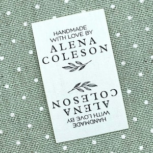 May include: A white rectangular tag with the text "HANDMADE WITH LOVE BY ALENA COLESON" in black. The tag also features a leaf design. The tag is on a green and white polka dot background.
