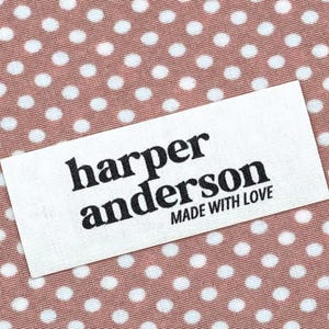 May include: A white rectangular label with the text "harper anderson MADE WITH LOVE" in black lettering. The label is set against a background of pink fabric with white polka dots.