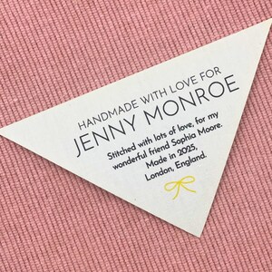 May include: A white triangular tag with the text "HANDMADE WITH LOVE FOR JENNY MONROE" in black. The tag also includes the text "Stitched with lots of love, for my wonderful friend Sophia Moore. Made in 2025, London, England."