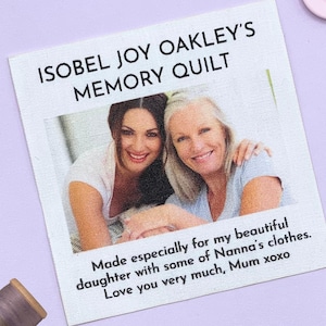 Könnte beinhalten: Ein weißes Stoffetikett mit dem Text "ISOBEL JOY OAKLEY'S MEMORY QUILT" und einem Foto von zwei lächelnden Frauen. Unter dem Foto steht der Text: "Made especially for my beautiful daughter with some of Nanna's clothes. Love you very much, Mum xoxo."