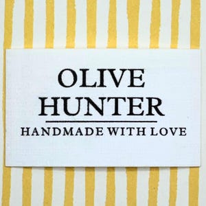 May include: A white rectangular label with the text "OLIVE HUNTER" in a bold, serif font, with "HANDMADE WITH LOVE" below. The background is a yellow and white striped pattern.