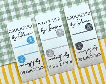 May include: Three white fabric labels with black text that reads "CROCHETED by Olivia" and "KNITTED by Imogen". Each label features a yarn ball graphic and a blue or gray line. The labels are on a green and yellow patterned background.