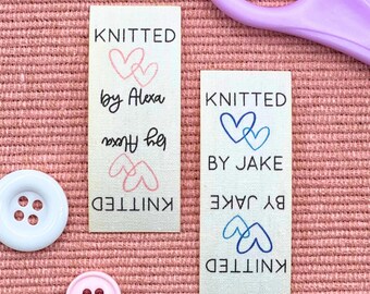 May include: Two rectangular fabric labels with the text "KNITTED" and "by Alexa" or "by Jake". Each label features a heart design. A white button and a pink button are also visible.