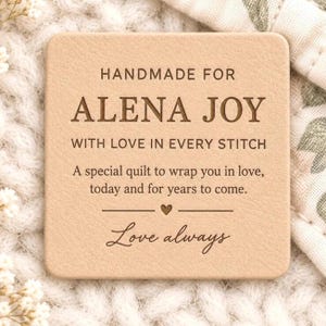 Puede incluir: Una etiqueta cuadrada de cuero color canela claro con esquinas redondeadas y texto grabado en marrón oscuro: HANDMADE FOR ALENA JOY WITH LOVE IN EVERY STITCH. A special quilt to wrap you in love, today and for years to come. Love always.