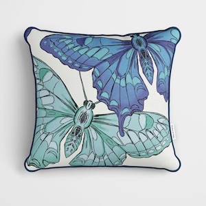 May include: A white cushion with a navy blue border features a design of two butterflies. One butterfly is blue and purple, and the other is light blue and green.