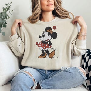 a woman sitting on a couch wearing a mickey mouse sweatshirt