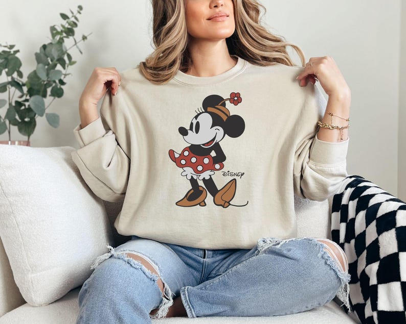 a woman sitting on a couch wearing a mickey mouse sweatshirt