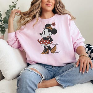 a woman sitting on a couch wearing a minnie mouse sweatshirt