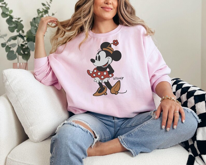 a woman sitting on a couch wearing a minnie mouse sweatshirt