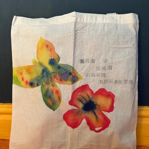 May include: A white tote bag with a watercolor butterfly and flower design. The text "NOT A LOT JUST FOREVER" is printed on the bag.
