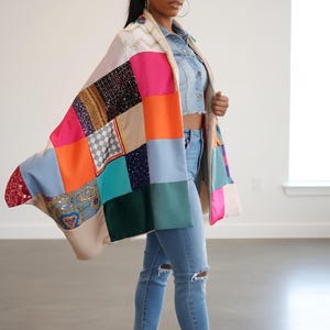 May include: A patchwork jacket with a variety of colorful squares, including pink, orange, and blue. The jacket is worn over a denim top and jeans. The outfit is completed with gold heels.