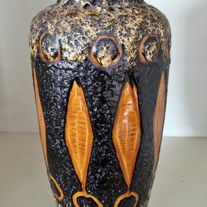 May include: A brown and black ceramic vase with a textured surface and a geometric pattern of orange and brown leaves. The vase has a speckled glaze.