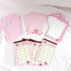 May include: A collection of pink stationery featuring the "Sugarbunnies" characters. The set includes notepads with various designs, including a weekly planner, dotted pages, and decorative borders. The stationery is adorned with cute illustrations and text.