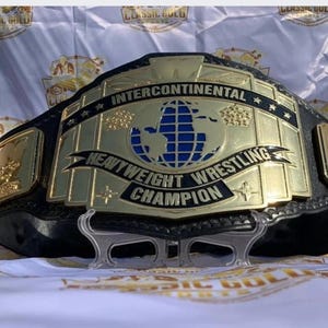 May include: A gold and black Intercontinental Heavyweight Wrestling Champion belt. The belt features a large central plate with a blue globe design and the words "Intercontinental Heavyweight Wrestling Champion".