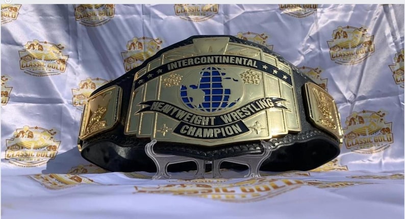 May include: A gold and black Intercontinental Heavyweight Wrestling Champion belt. The belt features a large central plate with a blue globe design and the words "Intercontinental Heavyweight Wrestling Champion".