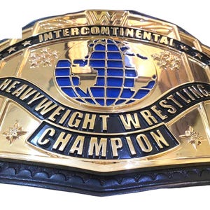 May include: A gold-colored wrestling championship belt with black and blue accents. The belt features the words "Intercontinental", "Heavyweight Wrestling Champion", and a blue globe design. The belt is made of leather and metal.
