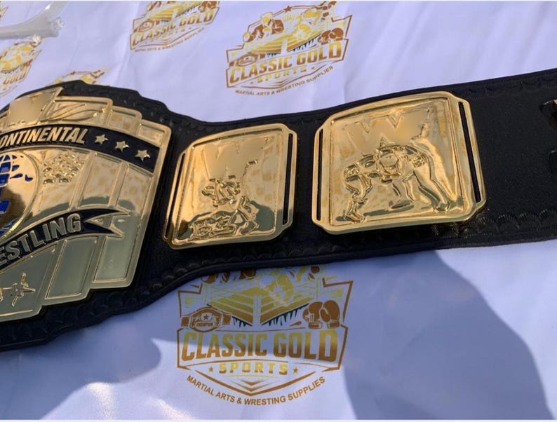 May include: A gold and black wrestling championship belt. The belt features gold plates with the words "Continental Wrestling" and images of wrestlers. The belt is made of black leather and has gold accents. The image also shows the Classic Gold Sports logo.