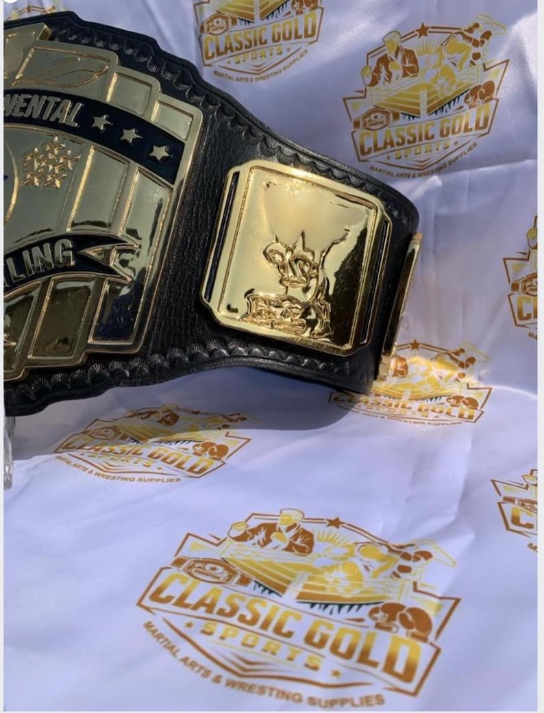 May include: A gold and black wrestling championship belt with the word "Continental" and stars on the main plate. The belt has a gold side plate with a figure. The background features a white cloth with the "Classic Gold Sports" logo.