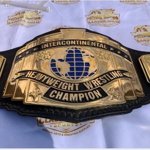 May include: A gold and black Intercontinental Heavyweight Wrestling Champion belt. The belt features a large central plate with a blue and gold globe design, and the words "Intercontinental Heavyweight Wrestling Champion".